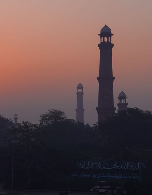 Silhouette of a mosque minaret and domes against a pink sunset sky in Lahore